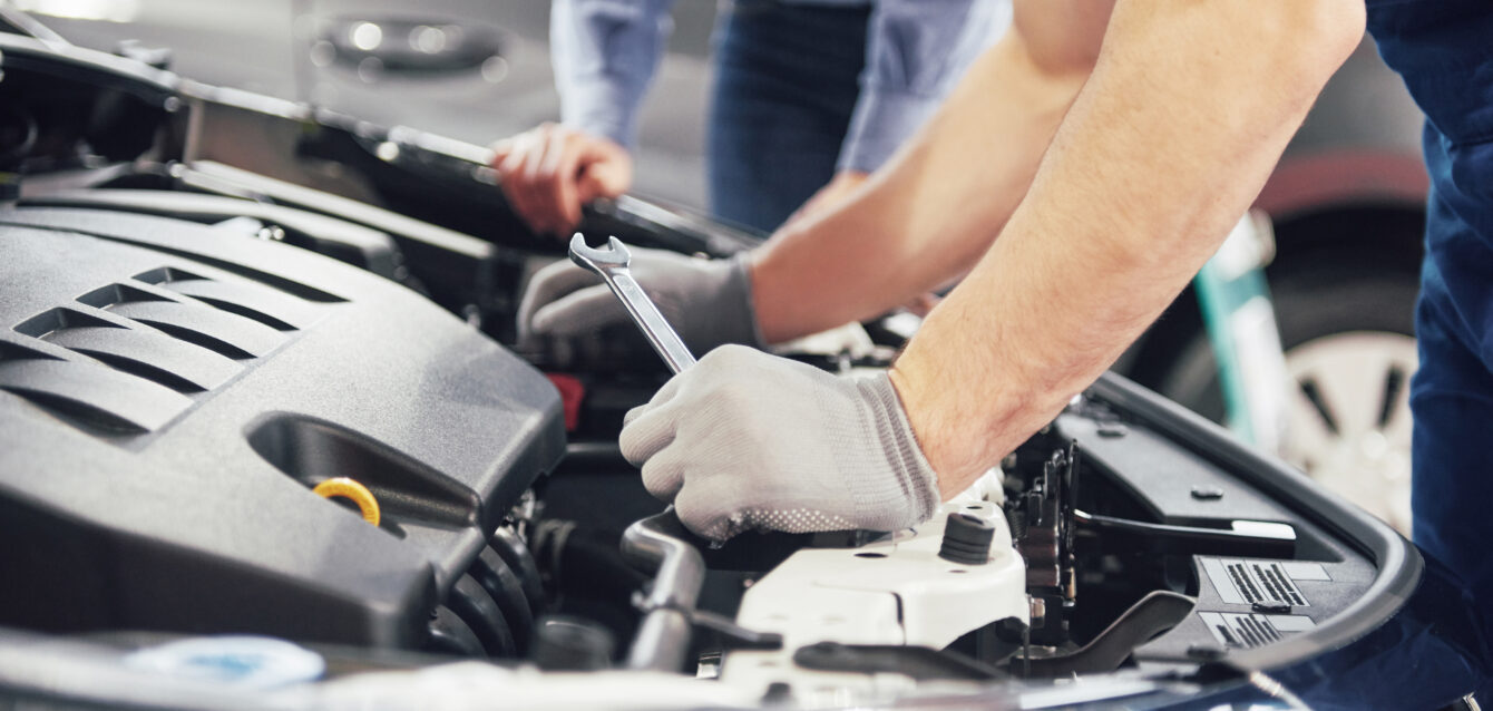 A man mechanic and woman customer look at the car hood and discuss repairs